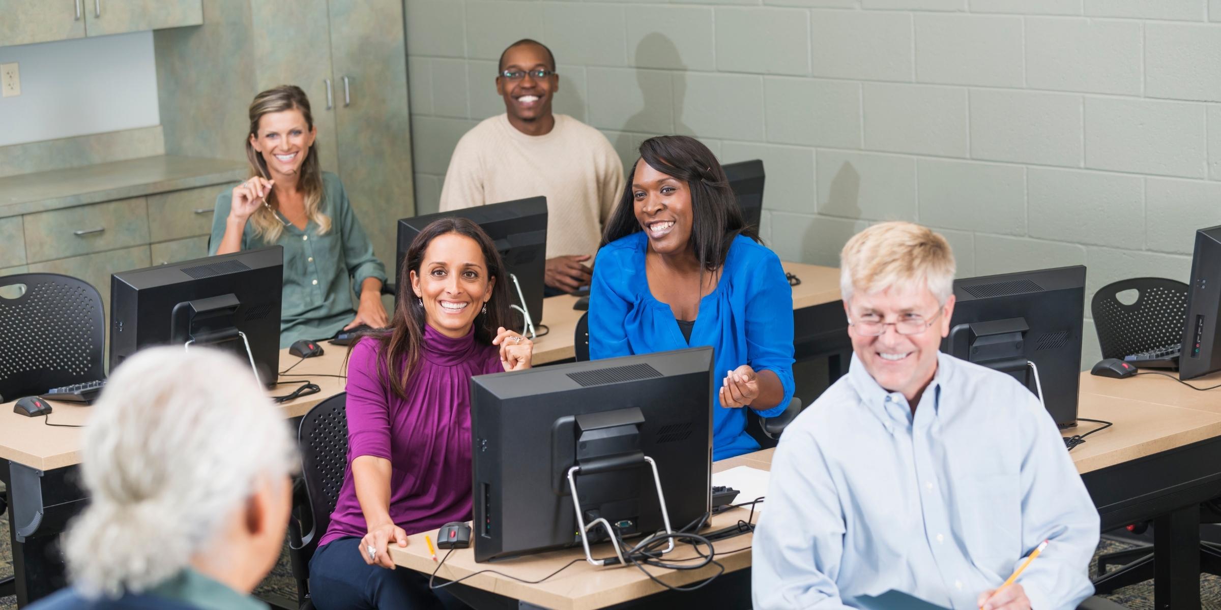 five adult learners in a classroom smiling at a teacher