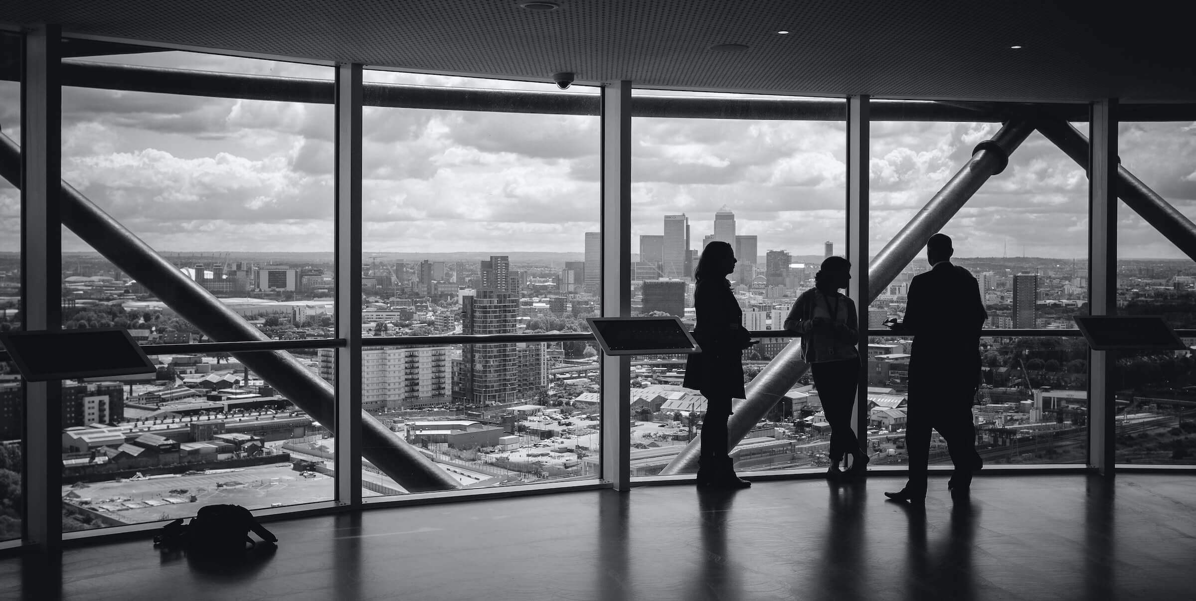 three people standing in large room overlooking a city