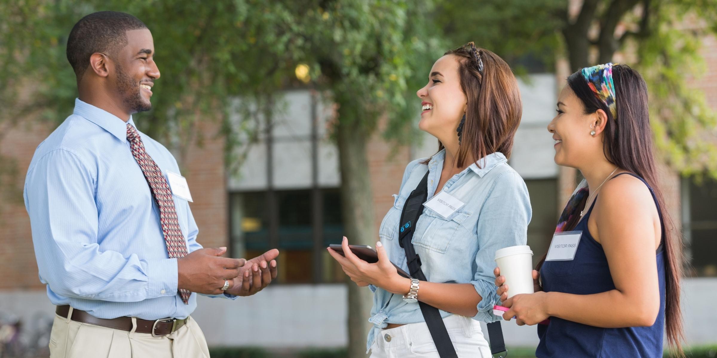 three people smiling and wearing nametags as they talk to each other on a sunny college campus