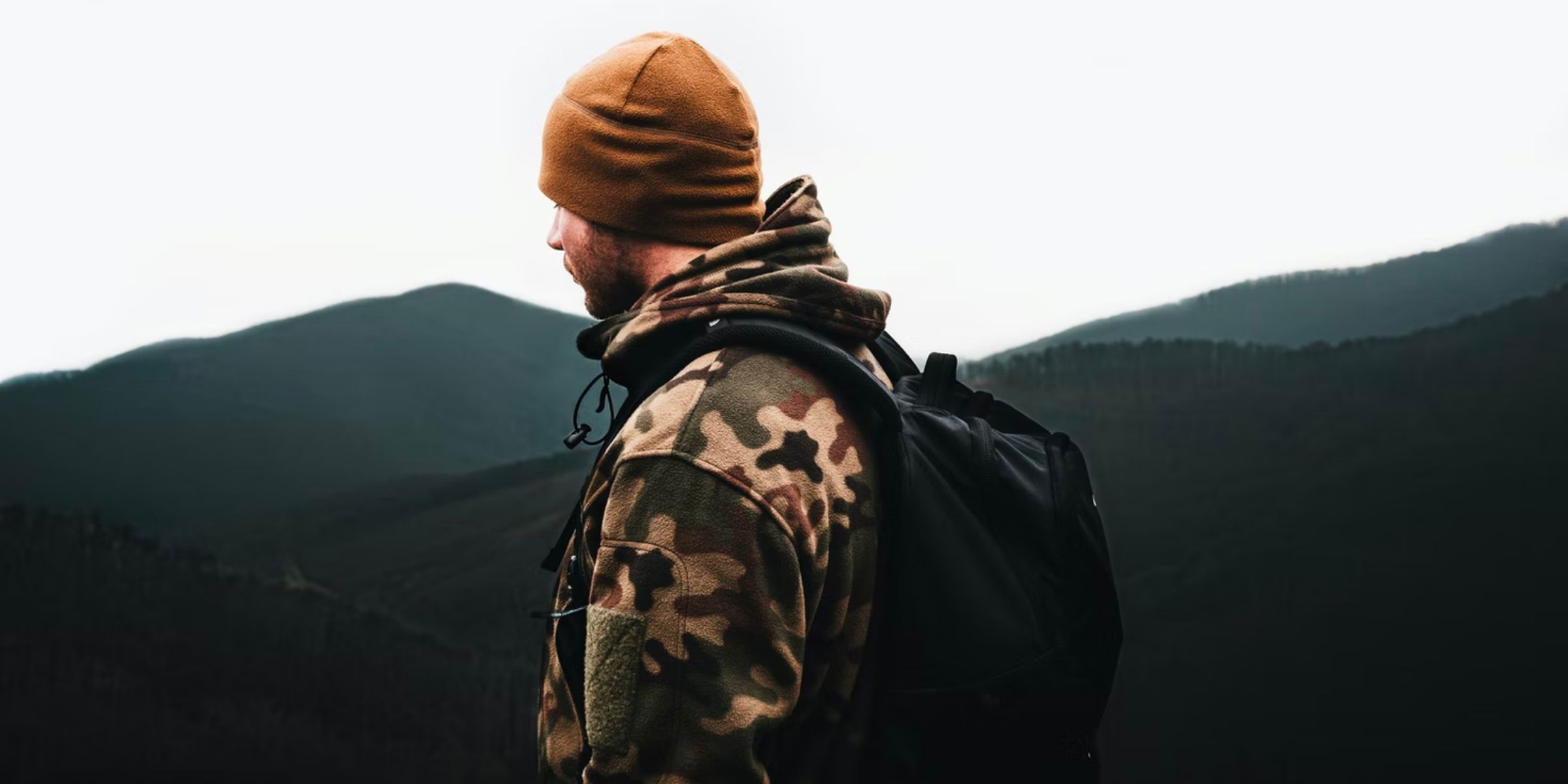 a person wearing a camouflage jacket standing on a mountain