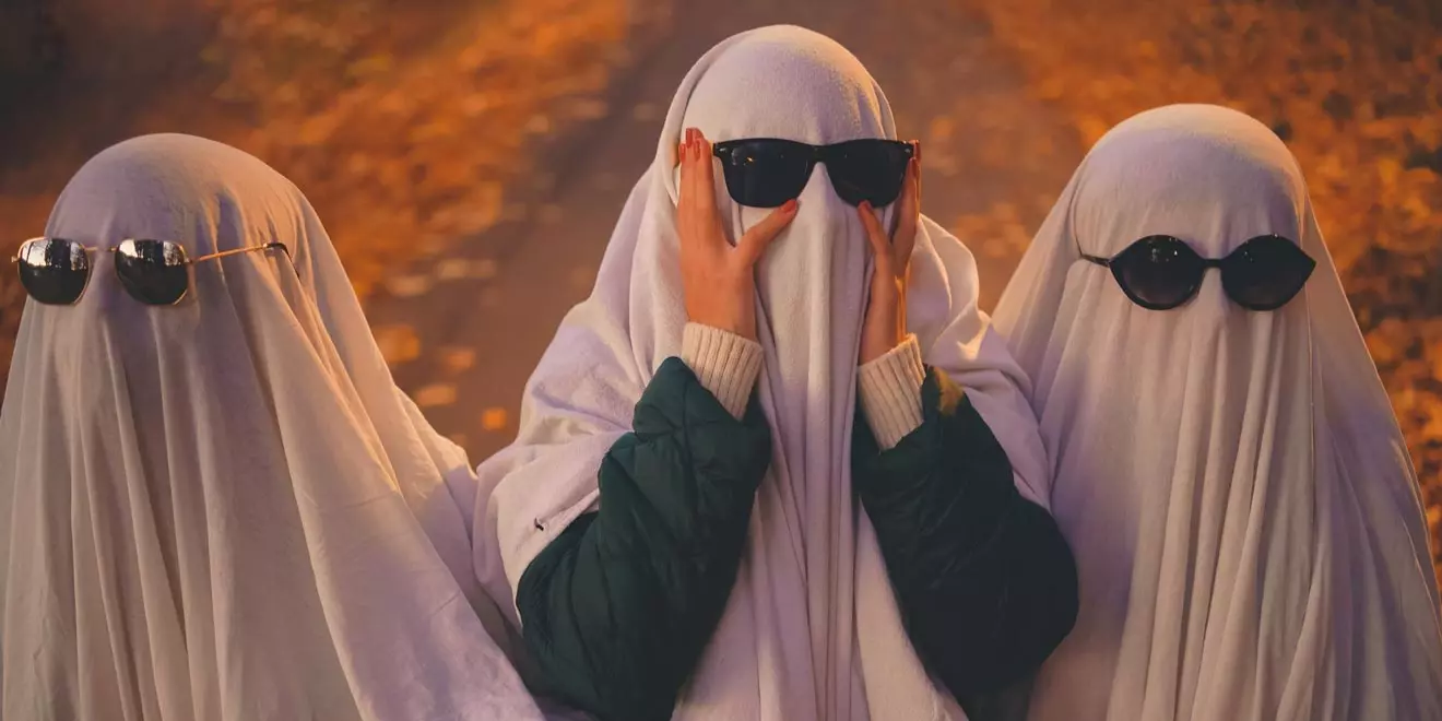 three people dressed as ghosts — covered in white sheets and wearing sunglasses on top