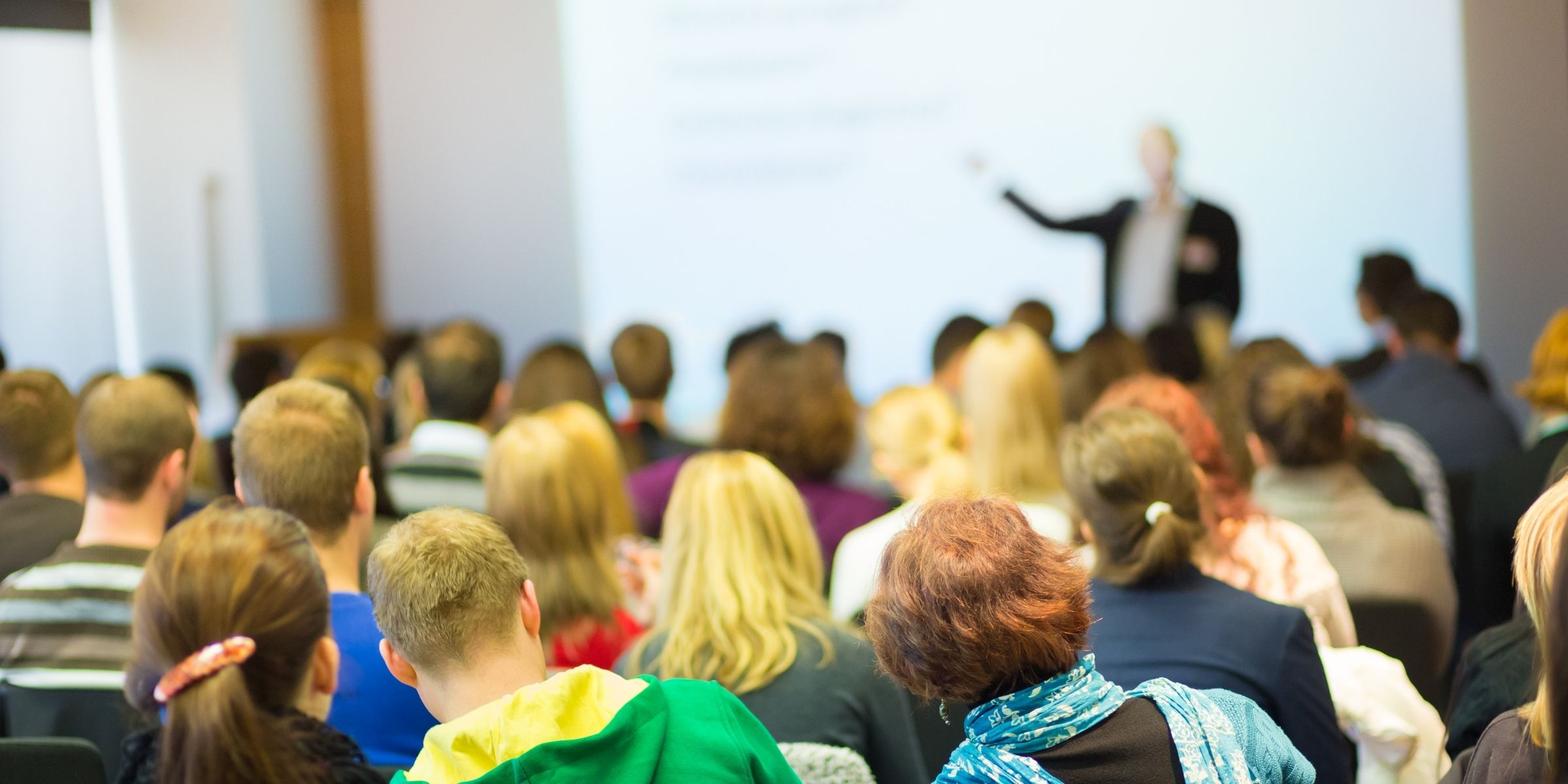 Students listening to an instructor at the front of a classroom