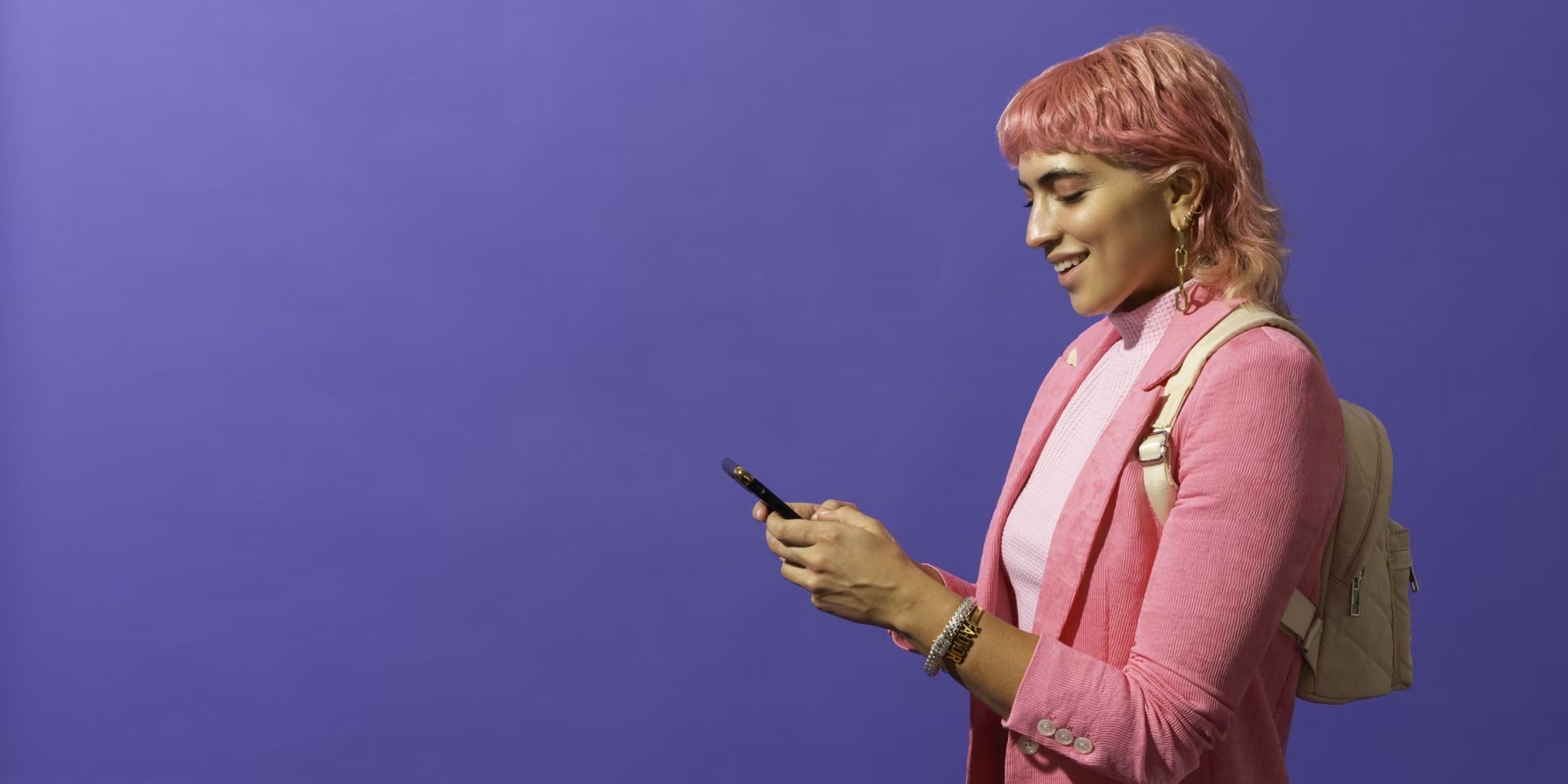 a student with pink hair and clothing smiling at their cell phone