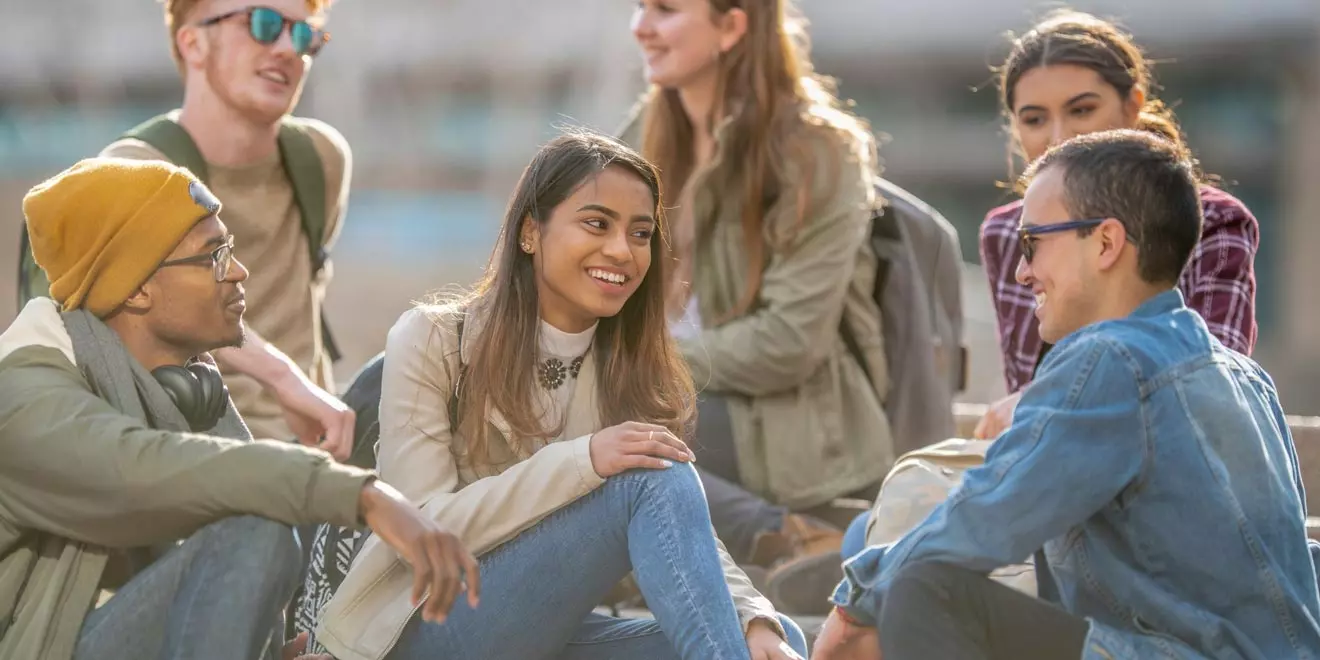 Group of six college students happily chatting with each other outside