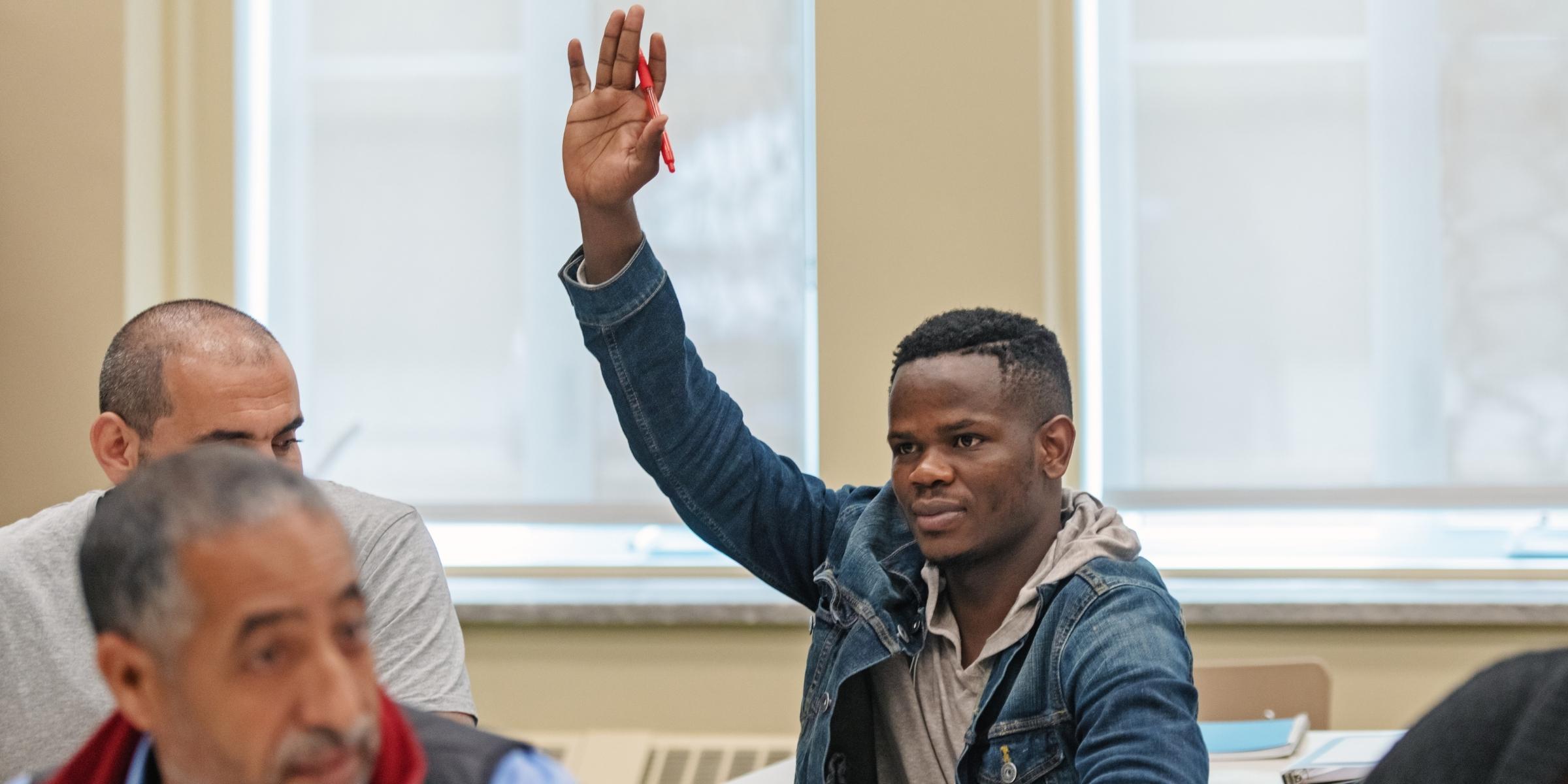 an adult student raising their hand inside a classroom with other adult learners