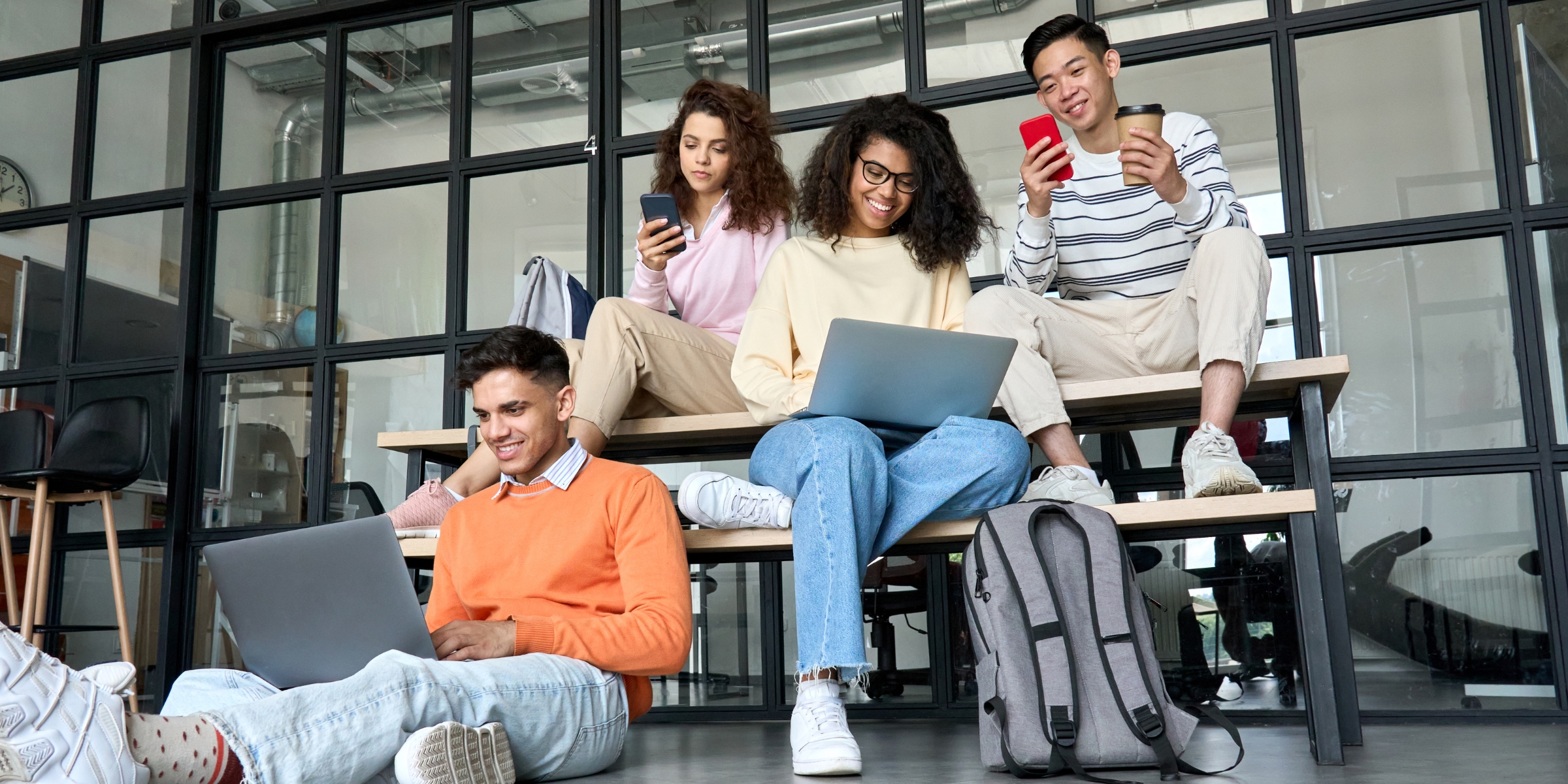 students sitting in a group and smiling at their laptops and cell phones